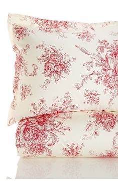 two red and white pillows with floral designs on them, one is folded up to the side