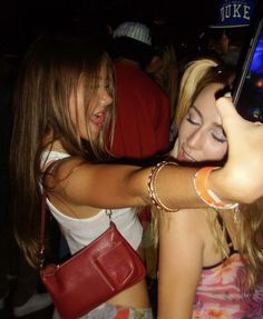 two young women taking pictures with their cell phones at a party in the night time