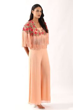 Peach cape crafted in net with all over multithread gul bahar embroidery and fringed hem detailing. Paired with a plain georgette blouse and flared pant. - Aza Fashions Spring Party Palazzo Set With Resham Embroidery, Spring Party Palazzo Set With Cape Sleeves, Fitted Tassel Sets For Spring, Spring Party Embroidered Palazzo Set, Fitted Sets With Tassels For Spring, Fitted Spring Sets With Tassels, Embroidered Sets With Cape Sleeves For Summer, Embroidered Summer Sets With Cape Sleeves, Spring Palazzo Set With Dupatta For Party