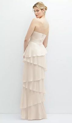 a woman in a strapless dress standing against a white wall with her back to the camera