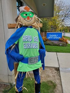 a scarecrow dressed in green and blue stands on the grass outside of a building