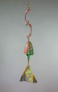 a glass bell hanging from a chain on a gray wall with a pink ribbon around it