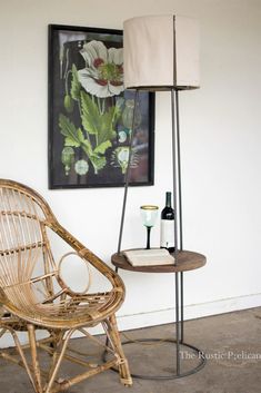 a wicker chair next to a table with a bottle of wine and a painting on the wall