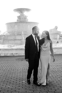 a man and woman standing next to each other in front of a fountain