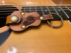 a guitar keychain with a leather case on top of an acoustic guitar strap