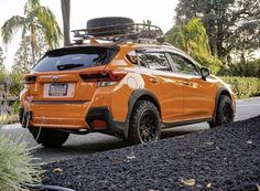 an orange subarunt is parked on the side of the road in front of some bushes