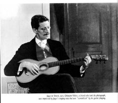 a black and white photo of a man holding a guitar in his right hand while sitting on a chair