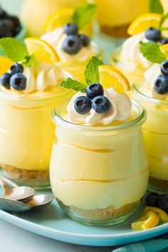 small desserts with lemon and blueberries in glass jars on a white plate next to spoons