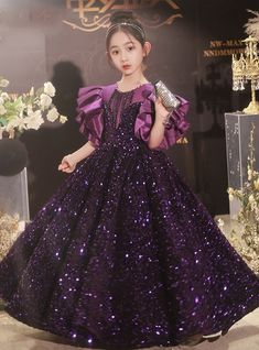 Acquiring a sense of majestic elegance is effortless with this stunning flower girl dress. The dress features a deep purple sequin-covered bodice that sparkles with every movement, making it a dazzling choice for any special occasion. The dramatic ruffled satin sleeves provide a regal touch, while the intricate beadwork at the neckline adds an extra layer of sophistication. The voluminous skirt flows beautifully, allowing for graceful movement and plenty of twirling. Perfect for weddings, pageants, or any formal event, this dress is designed to make a lasting impression. The high-quality construction ensures durability and comfort, with a soft inner lining that will keep your little one comfortable all day long. An easy-to-use zipper and adjustable fit make dressing simple and convenient. Elegant Purple Princess Dress For Prom, Purple Embellished Pageant Dress, Purple Embellished Dress For Pageant, Purple Sequin Dress For Prom Season, Purple Sequin Dress For Prom, Purple Embellished Ball Gown For Party, Embellished Purple Ball Gown For Party, Purple Ruffled Ball Gown For Pageant, Purple Sequin Ball Gown Dress