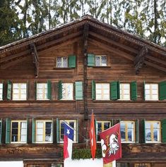 a large wooden building with green shutters and flags