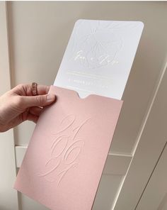 a person holding up a pink and white wedding card with the word love on it