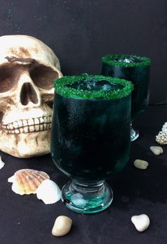 two glasses filled with green liquid next to a skull