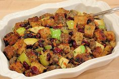 a white bowl filled with stuffing and fruit on top of a wooden table next to a fork