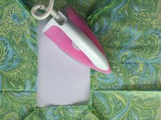 a pink and white electric iron sitting on top of a green paisley cloth covered bed