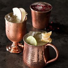 two copper mugs filled with drinks and garnished with fruit