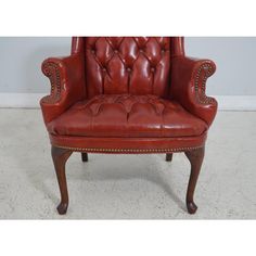 a red leather chair sitting on top of a white carpeted floor next to a wall