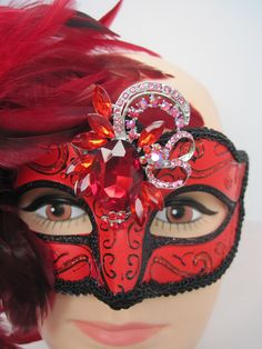 * Generous and red and black fluffy feathers over the right side of the face in this design. The feathers pick up the black braided trim around the mask and the black glitter eye liner. In addition the asymetrical faceted red crystal medallion adds more drama to the mask. * To secure the mask there are black satin ribbons to tie in the back of the head. The ribbons can be cut as I always include plenty of length. This mask will fit any size head and looks great on any age as well. * A great piec Mask With Feathers, Venetian Masquerade Masks, Masked Ball, Venetian Masquerade, Glitter Eye, Back Of The Head, Satin Ribbons, Glitter Eyes, Masquerade Mask