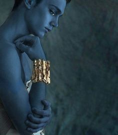 a man with blue skin and gold bracelets on his arm looking down at the ground