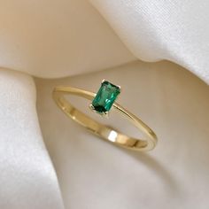 a gold ring with an emerald colored stone on it's side and white fabric in the background