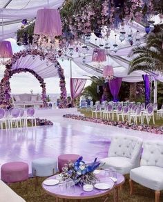 an outdoor wedding venue decorated with purple and white flowers, chandeliers and chairs