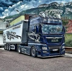 a blue semi truck parked in front of a building with mountains in the back ground