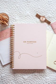 an open notebook sitting on top of a bed next to a watch and other items