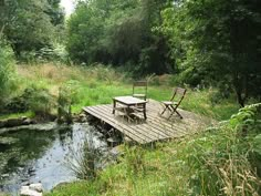 there is a picnic table and chairs on the dock by the river in the woods