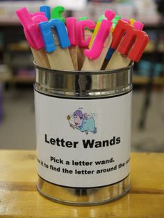 a tin filled with colorful letters sitting on top of a wooden table next to a phone