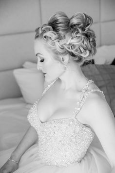 black and white photograph of a woman in a wedding dress sitting on a bed with pillows