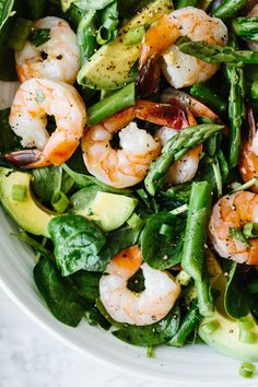 a white bowl filled with shrimp, avocado and spinach on top of a table