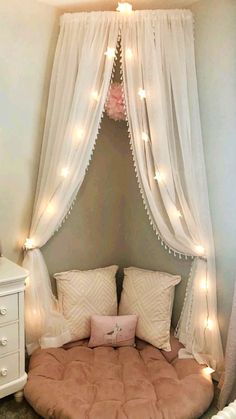 a round bed with white curtains and lights hanging from it's sides in a bedroom