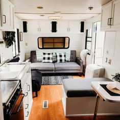 a living room and kitchen area in a mobile home with white cabinets, wood flooring and gray couches