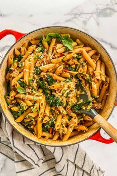 a pot filled with pasta and spinach on top of a white marble countertop