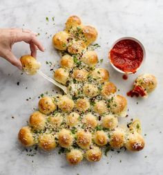 a christmas tree made out of bread with sauce on the side and hands reaching for it