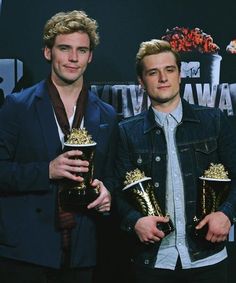 two young men standing next to each other holding trophies