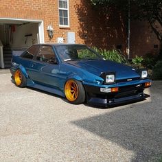 a blue car parked in front of a brick building with yellow rims on it