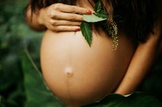 a pregnant woman's belly is covered with leaves and flowers, while her hands are on the stomach