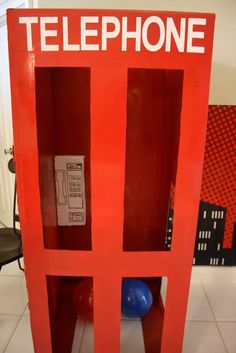 a red phone booth sitting on top of a white tile floor next to a blue ball