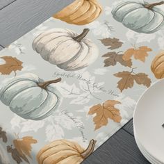 a place mat with pumpkins and leaves on it, next to a white plate