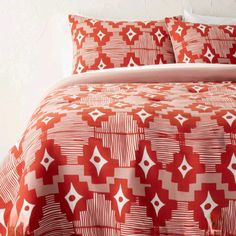 a bed with red and white bedspread, pillows and pillow cases on it