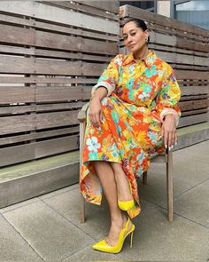 a woman sitting on a wooden bench wearing yellow high heels and a colorful floral dress