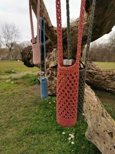 three crocheted bags hanging from a tree branch in the grass with chains attached to them