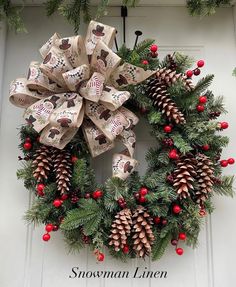 a christmas wreath with pine cones and red berries on the front door is adorned with an ornament