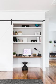 a computer desk sitting in front of a white book shelf filled with books and other items