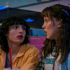 two women sitting next to each other with drinks in front of their faces and looking at the camera