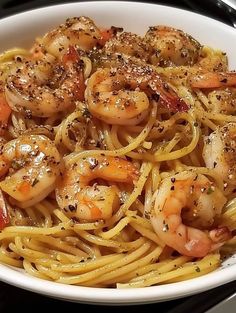 a white bowl filled with pasta and shrimp on top of a black stove burner