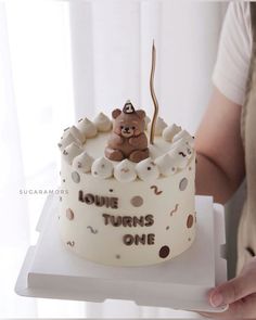 a person holding a cake with a teddy bear on it and the words louis turns one