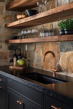 a kitchen with stone walls and black cabinets, copper faucet, glassware on the shelves