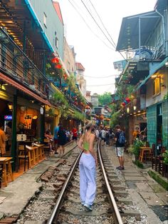 people are walking on the railroad tracks in an alleyway with shops and restaurants lining both sides