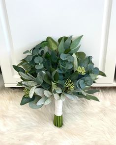 a bouquet of green leaves and greenery sits on a white furnishing next to a door